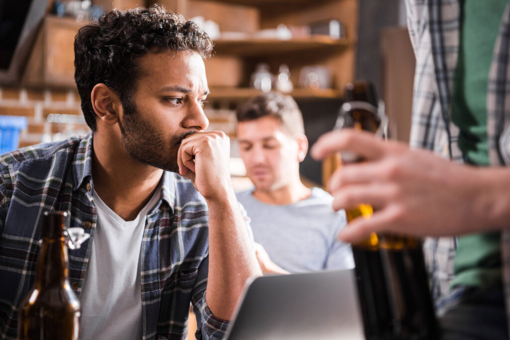 Serious young man using a laptop while friends are drinking.