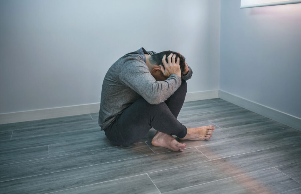 Man sitting on an empty room holding his head.