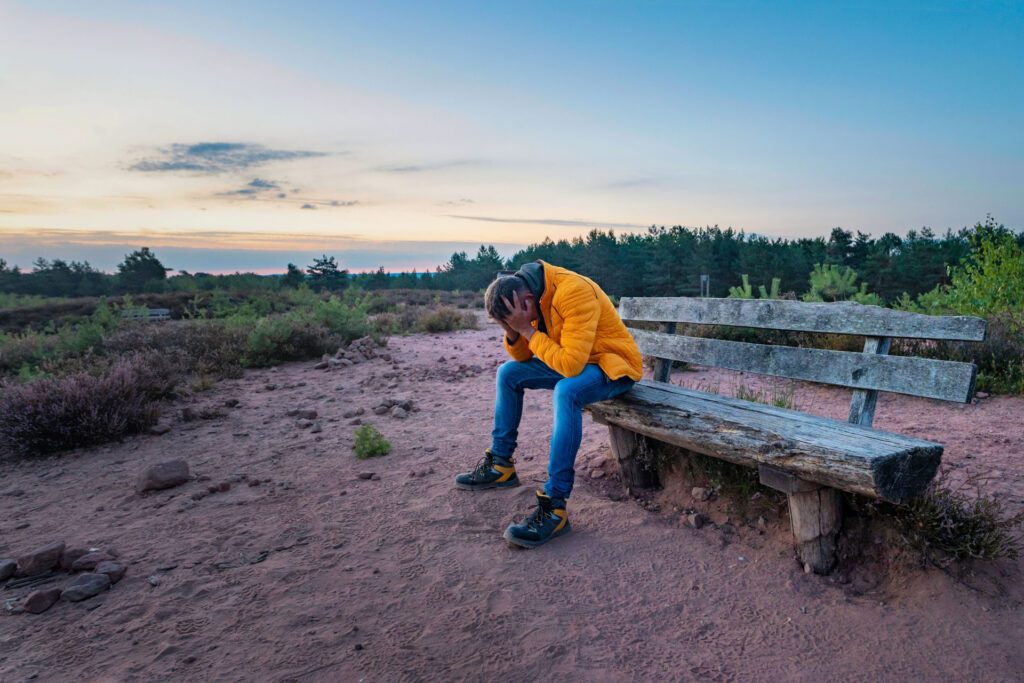 Man with depression sitting on a bench outdoor.