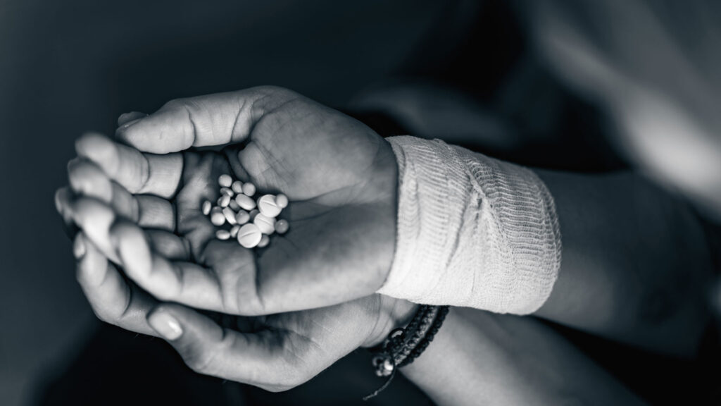 Hands of a person with opioid addiction holding medicines.