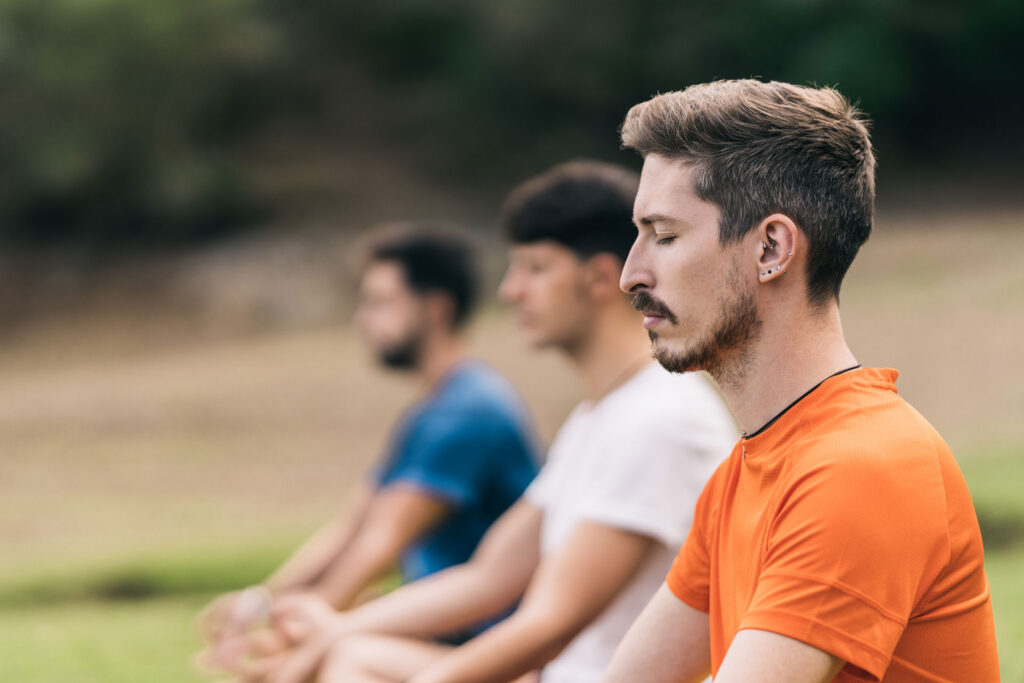 Three men doing meditation outdoors.