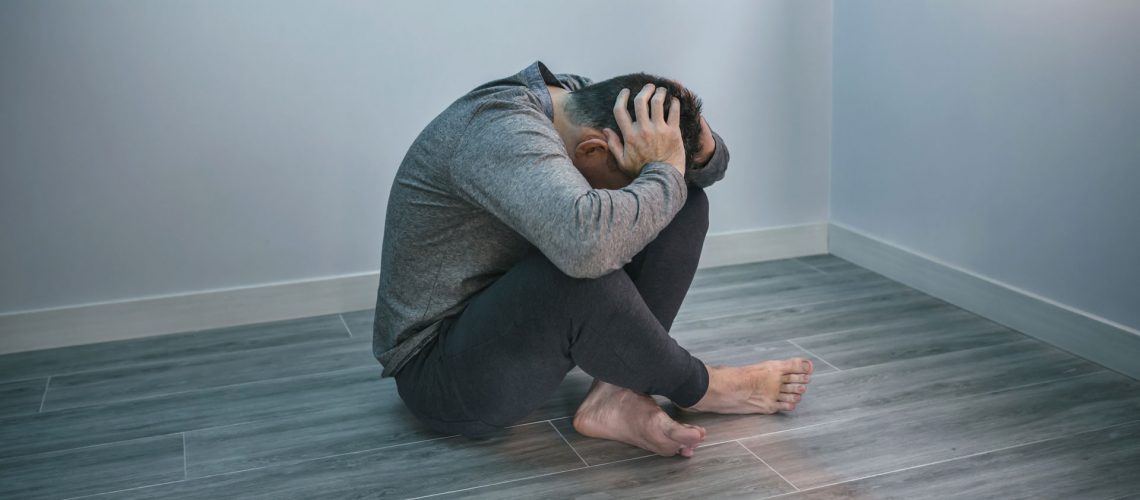 Man sitting on an empty room holding his head.