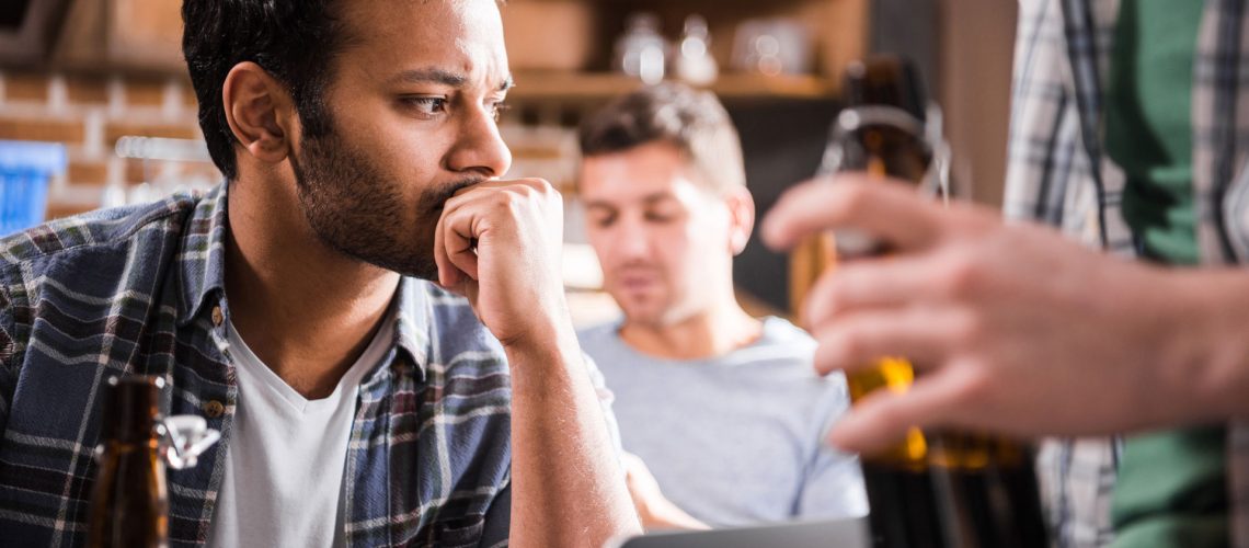 Serious young man using a laptop while friends are drinking.